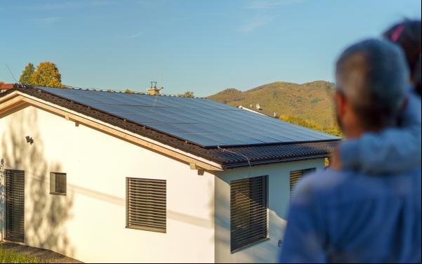Vista trasera de un padre con su hija en brazos y mirando su casa con es solares instalados.